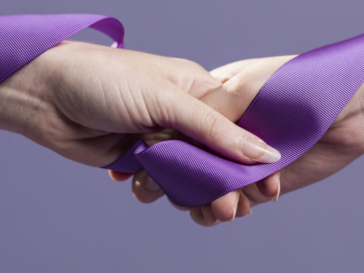 women hands holding purple ribbon